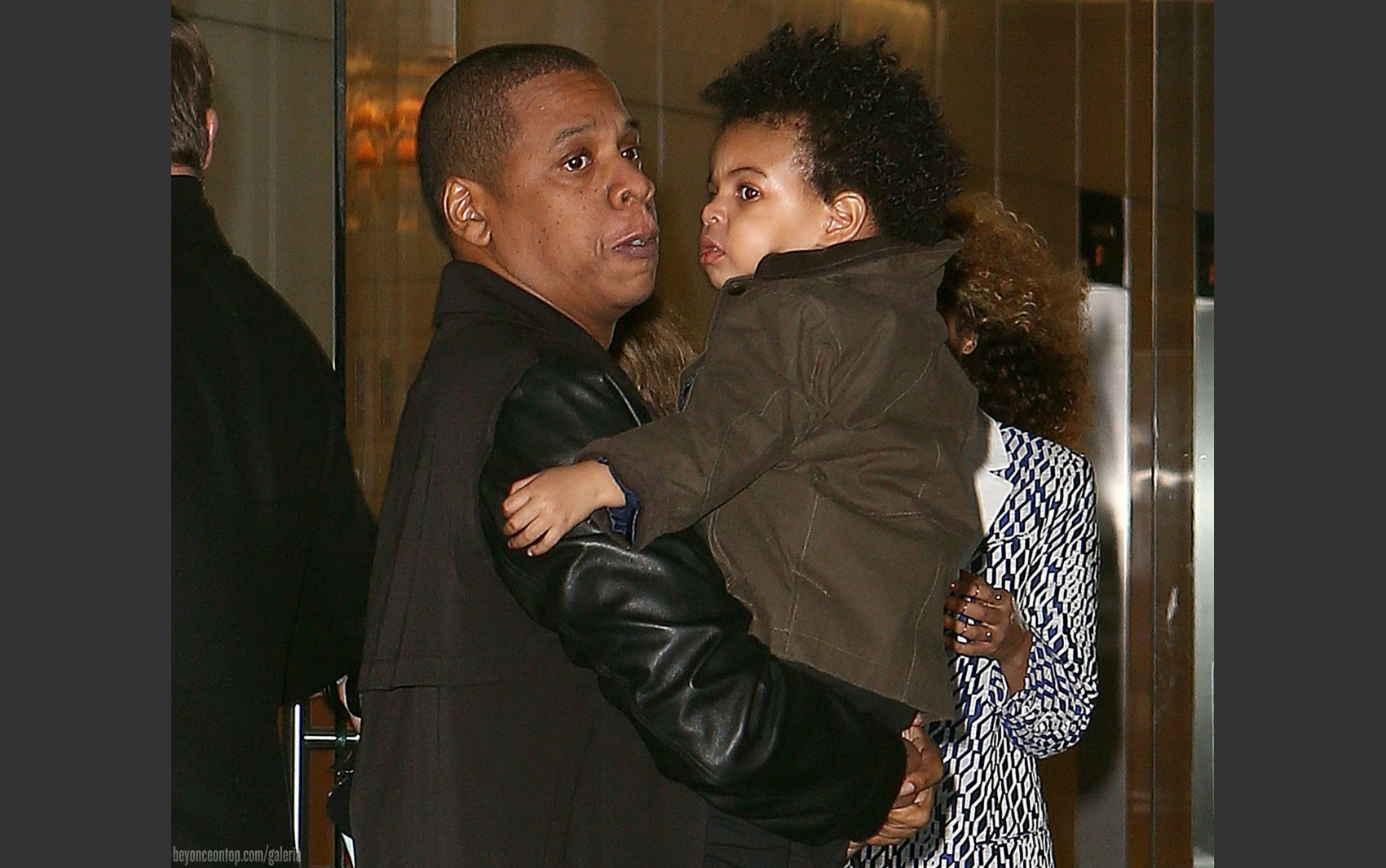 Jay-Z carrega Blue Ivy. Beyonc&eacute; ao fundo.